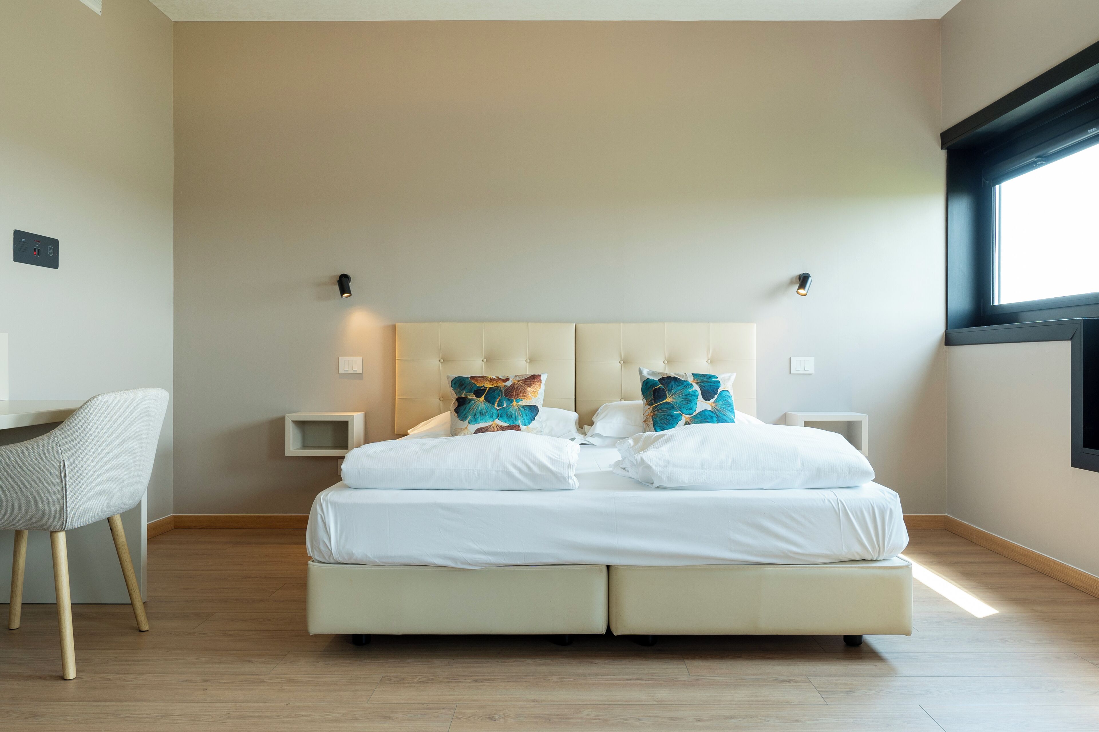 A modern bedroom with a large bed, bedside tables, a desk, and a window.