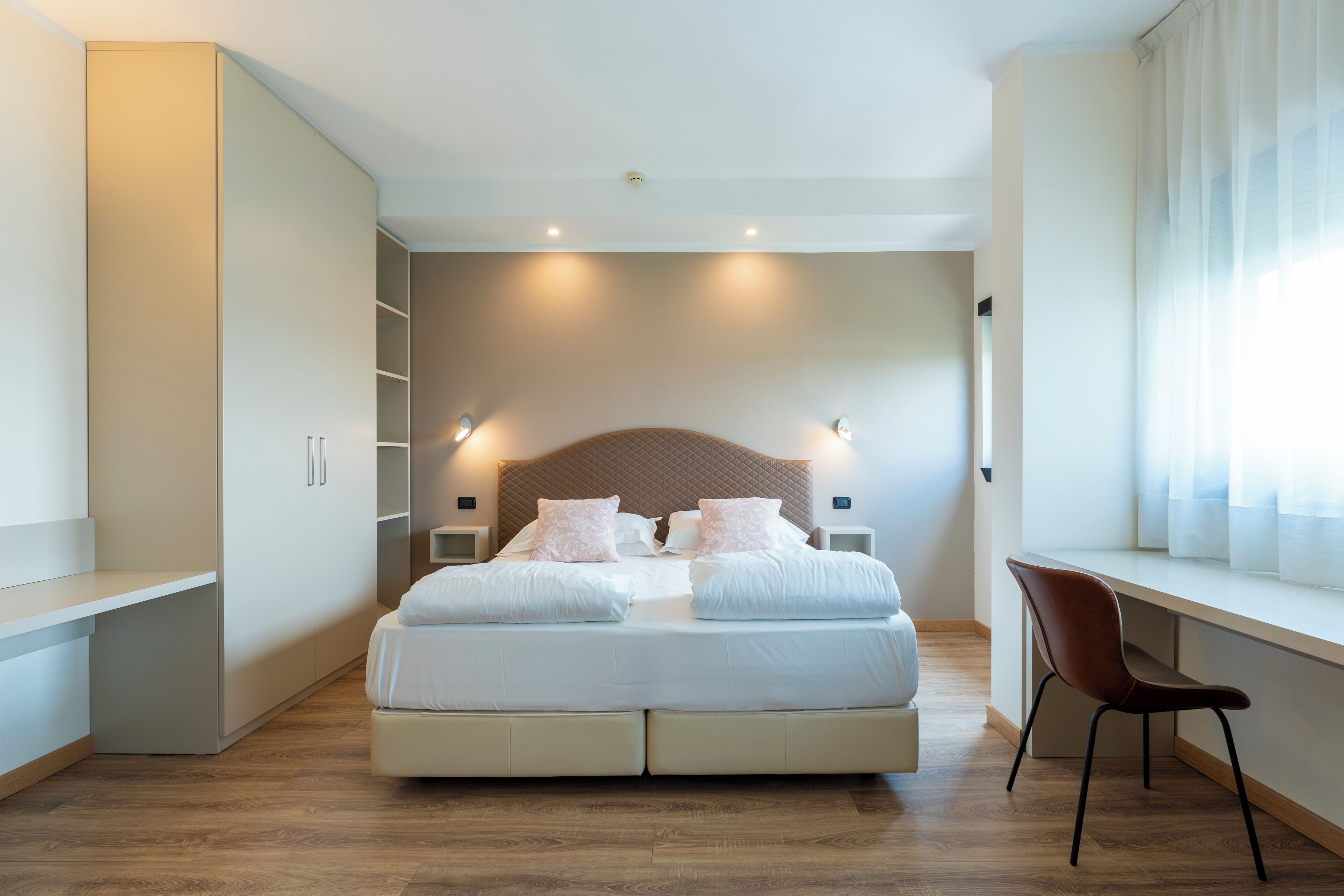 Een moderne slaapkamer met een groot bed, een inbouwkast, nachtlampjes en een raam met gordijnen.