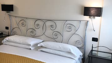 A neatly made bed with white linens and a patterned bedspread, a metal headboard with decorative swirls, two bedside tables with lamps, and a small black nightstand.