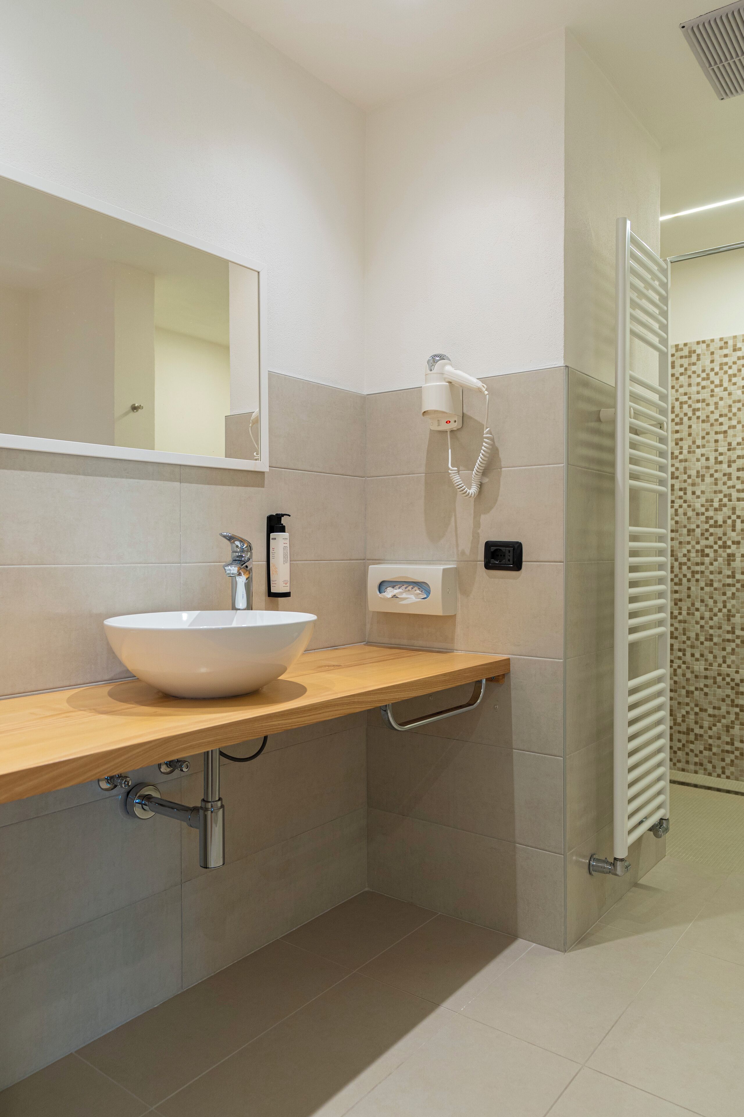 Un bagno moderno con un ampio lavandino bianco, uno specchio, un porta asciugamani e una zona doccia.