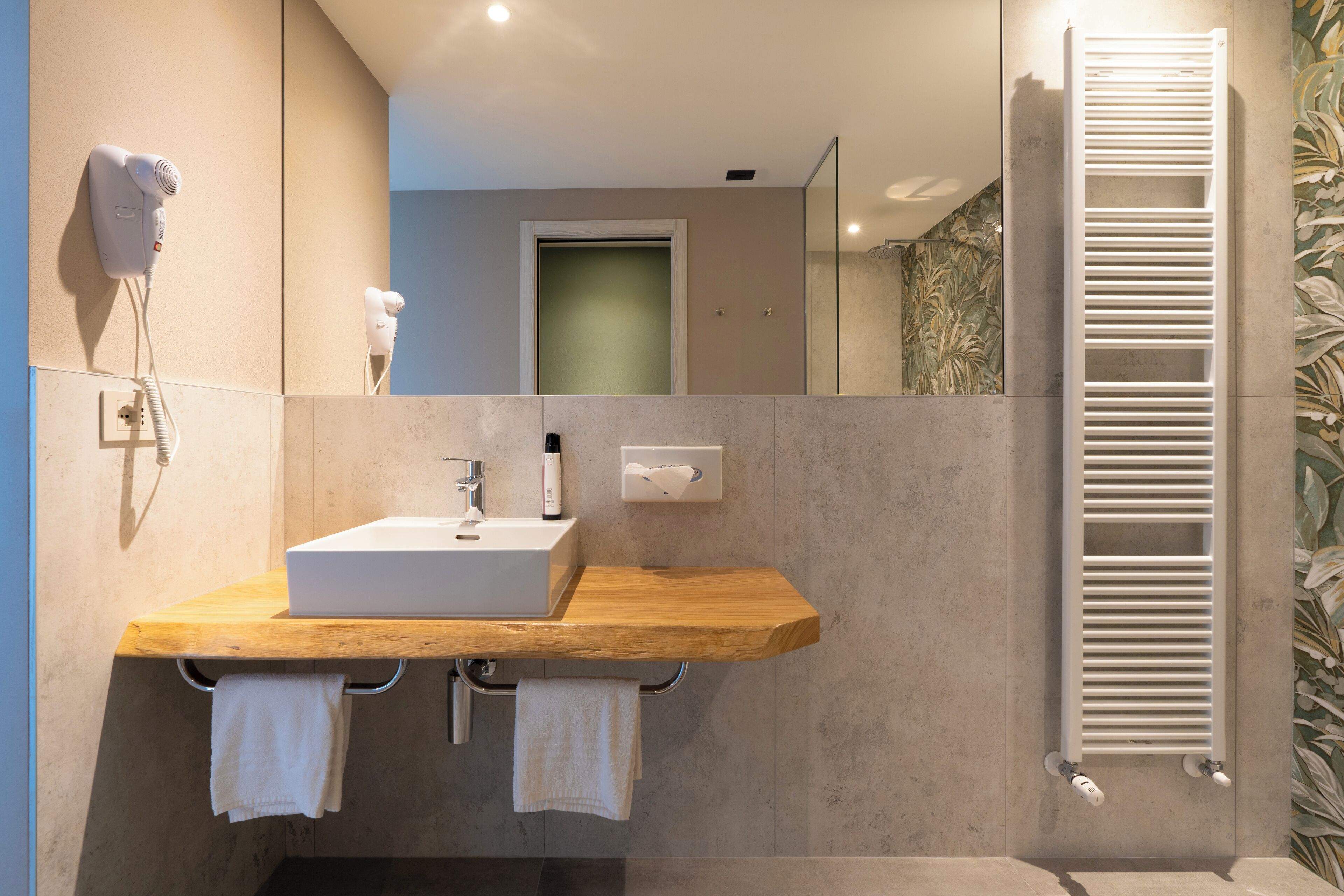 Un baño moderno con tocador de madera, lavamanos integrado, toallero, secador de pelo y dispensador de toallas.