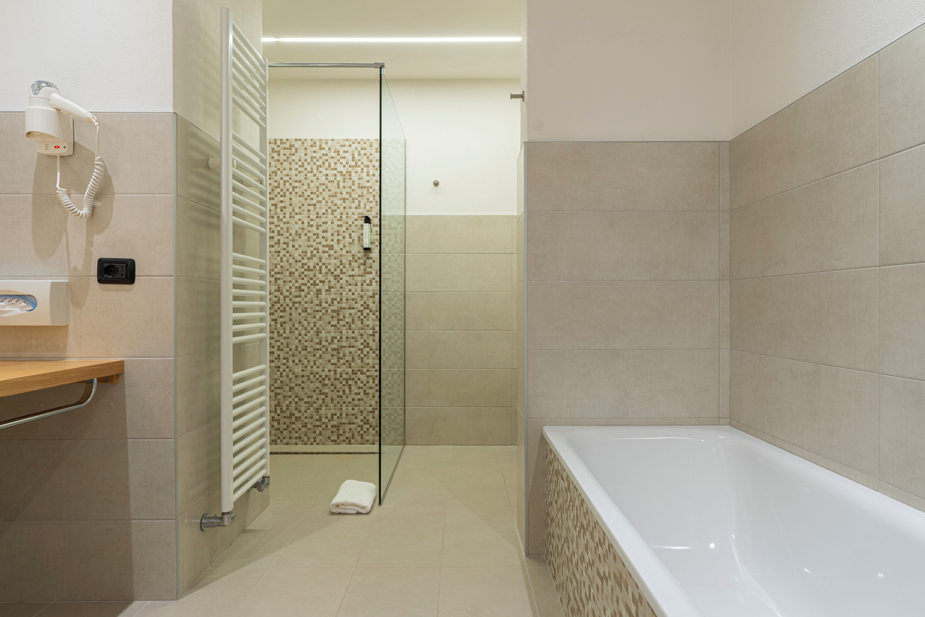 A modern bathroom with a walk-in shower, a bathtub, and a hairdryer on the wall.