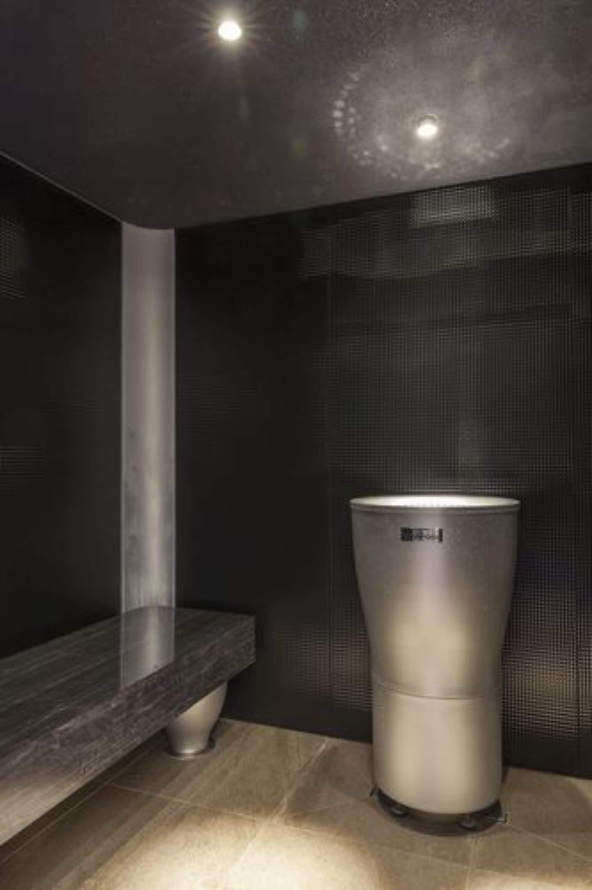 Un baño moderno con pared de azulejos oscuros, encimera de mármol y un lavabo cilíndrico.