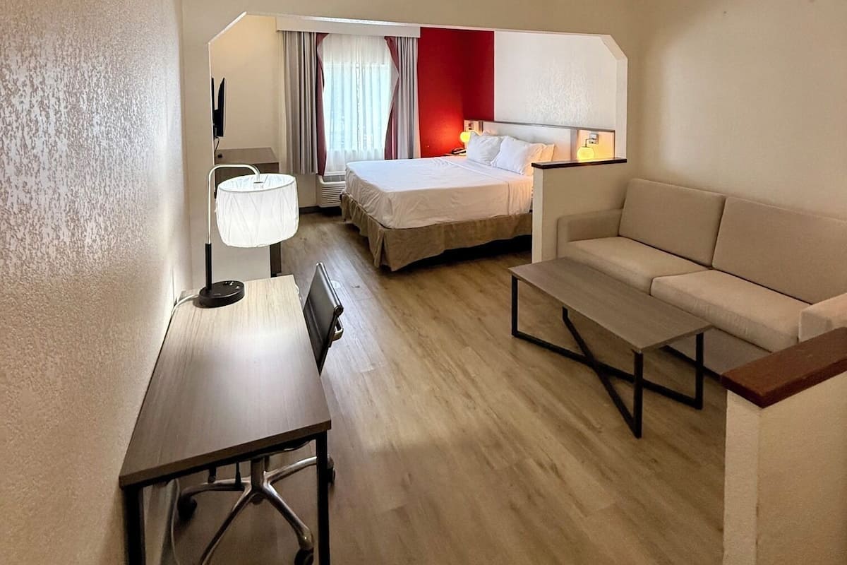 A hotel room with a bed, a desk, a sofa, and a window with curtains.
