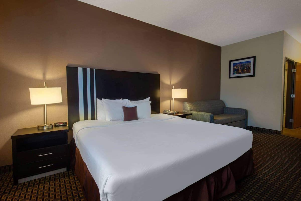 A hotel room with a large bed, two bedside tables with lamps, a sofa, and a framed picture on the wall.