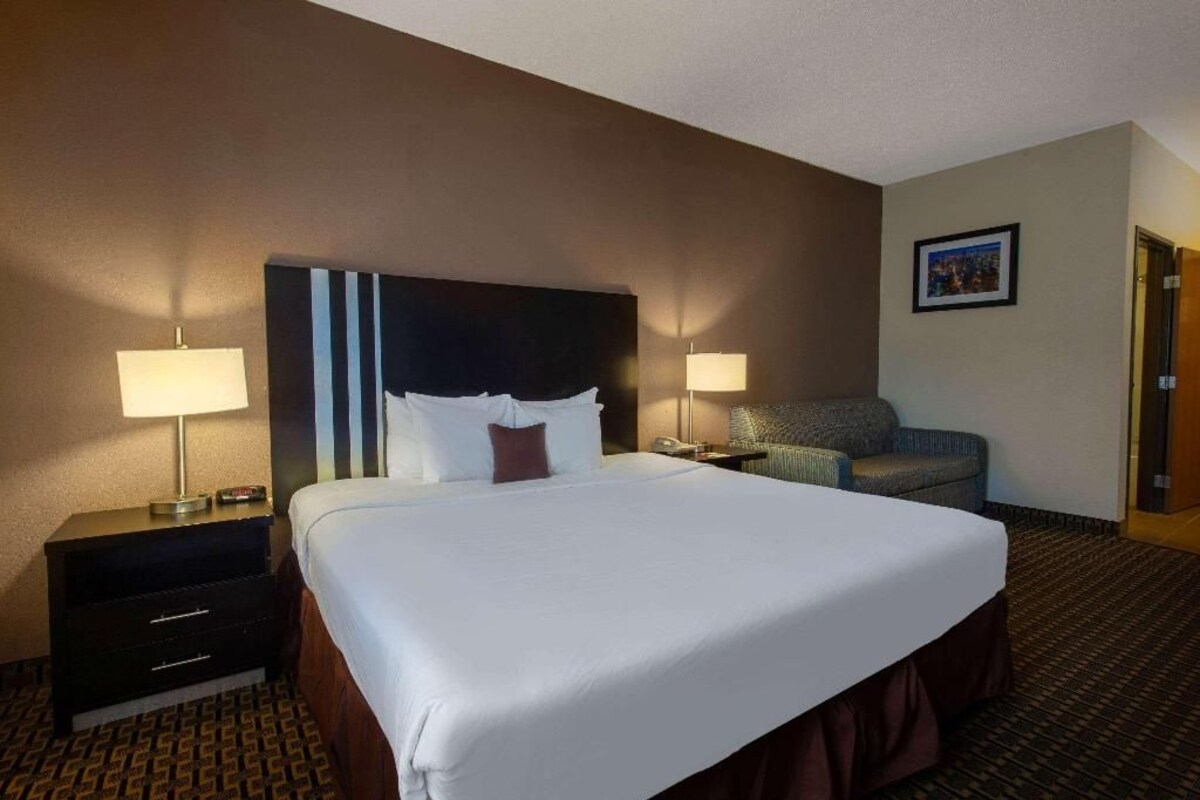 Una habitación de hotel con una cama grande, dos mesitas de noche con lámparas, una silla y un cuadro enmarcado en la pared.