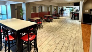 A spacious indoor area with multiple tables and chairs, a kitchen area, and a seating area with red cushions.