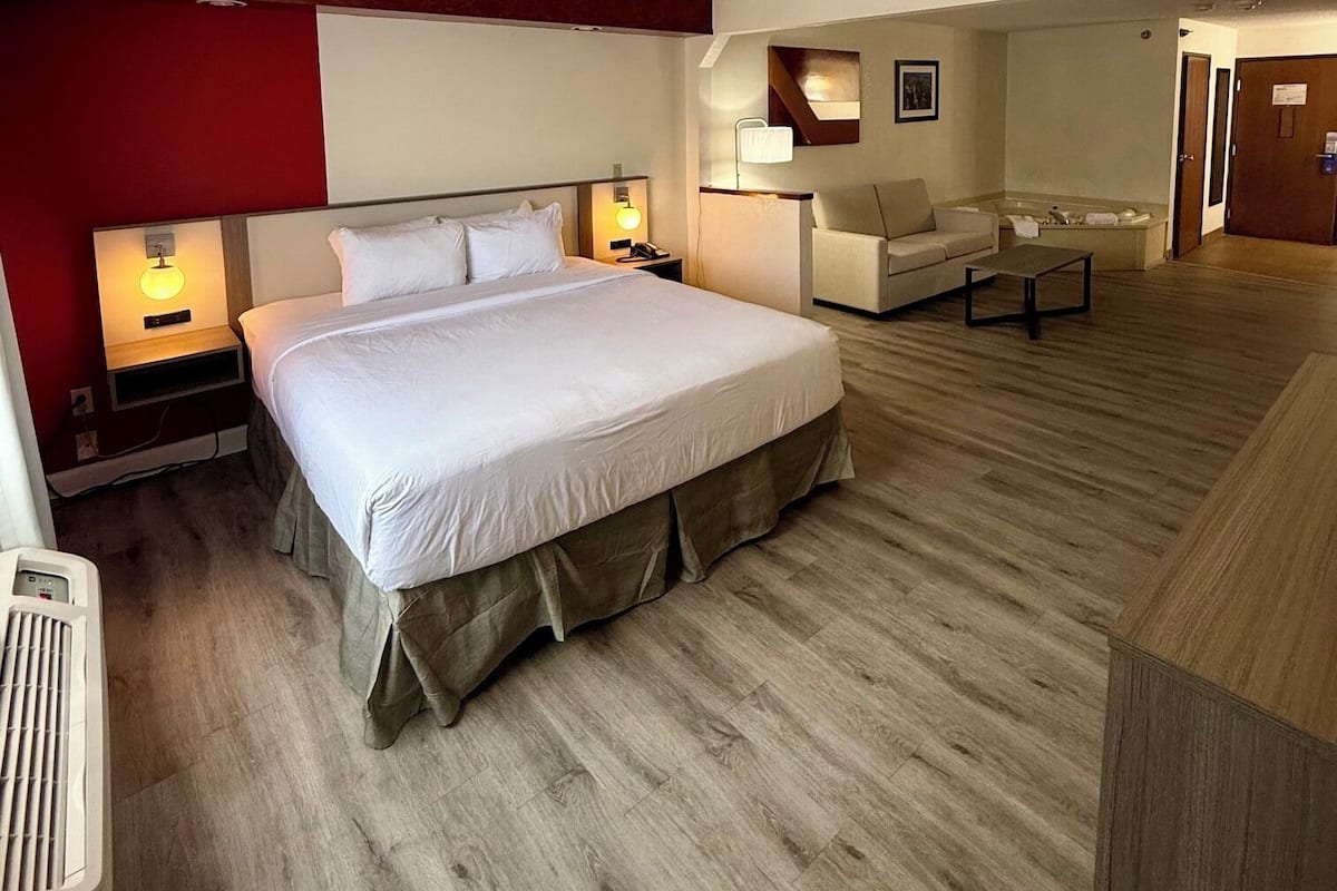A hotel room with a large bed, bedside tables, a desk, a chair, and a mirror.