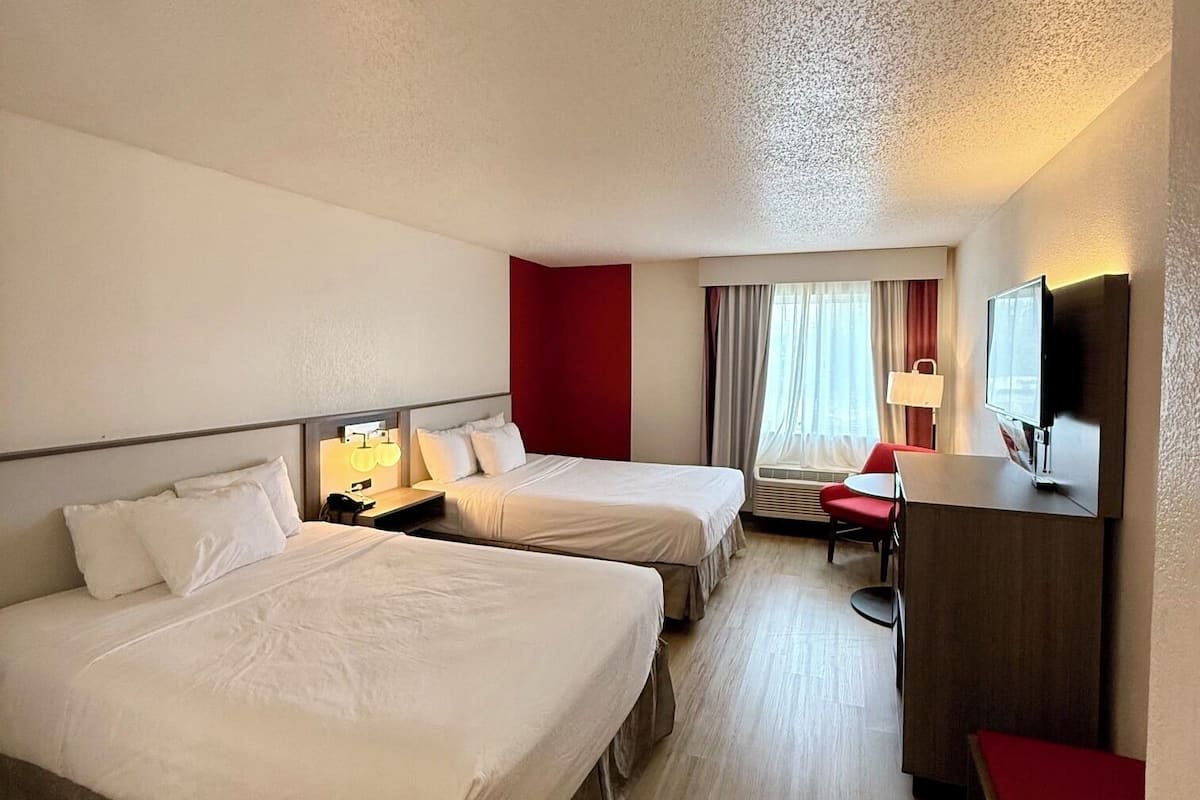 A hotel room with two beds, a desk, a chair, a TV, and a window with curtains.