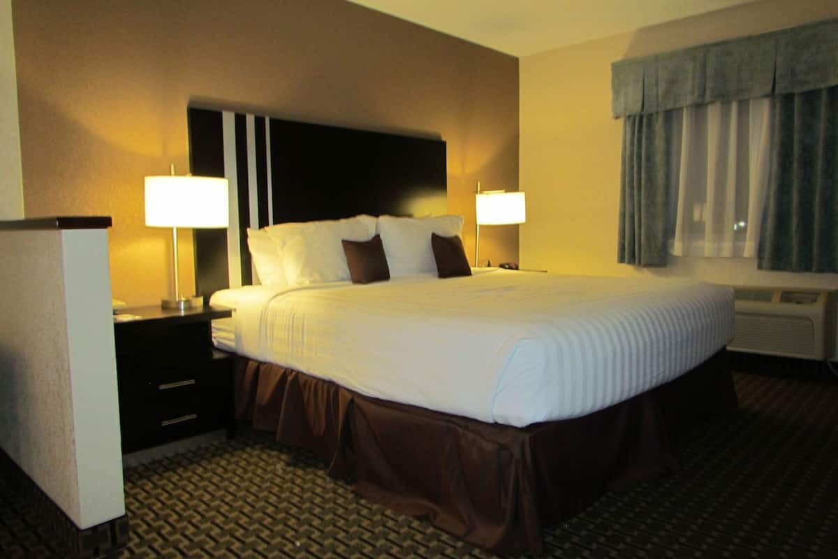 A hotel room with a large bed, two bedside lamps, a nightstand, a dresser, and a window with curtains.