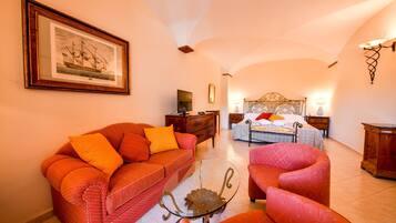 Quarto de hotel com cama, sofá, poltrona, mesinha, cómoda, espelho e um quadro na parede.
