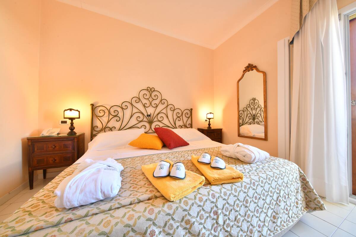 A hotel room with a bed, two bedside tables, a mirror, and a window with curtains.