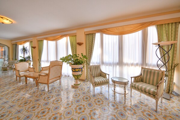 A spacious room with a patterned floor, multiple seating options including a sofa and armchairs, a potted plant, and a floor lamp.