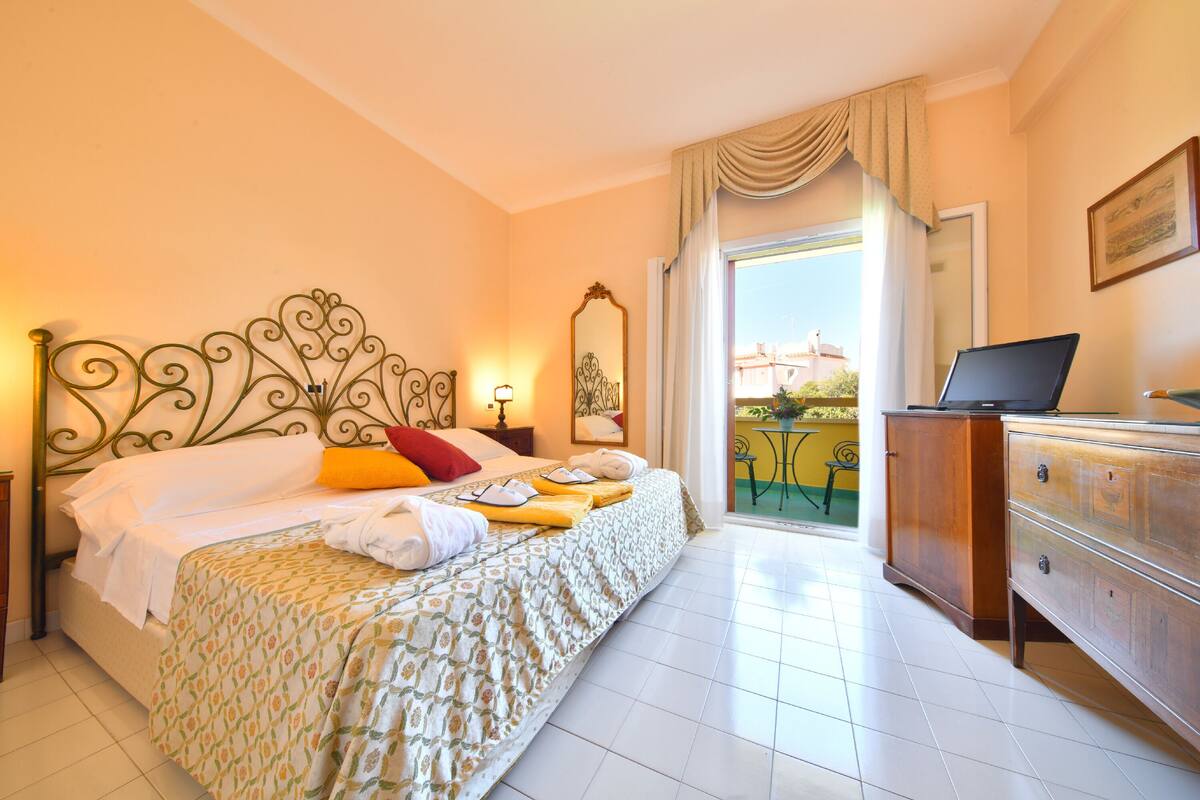 Een hotelkamer met een bed, een bureau met een laptop, een dressoir en een balkon met uitzicht.