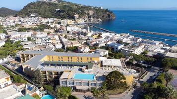 Vista aérea de uma vila costeira com edifícios, piscina e um cais.