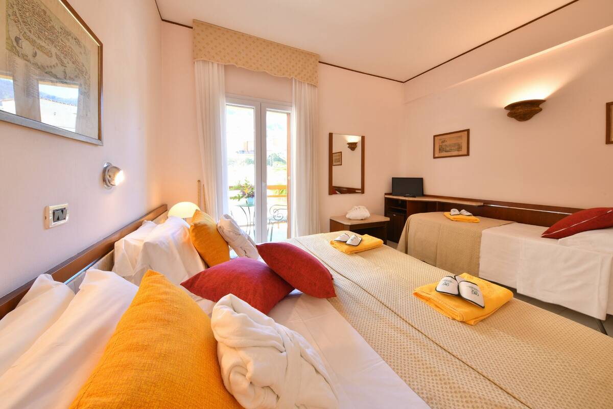Een hotelkamer met twee bedden, een balkon, een bureau met stoel, en een televisie.