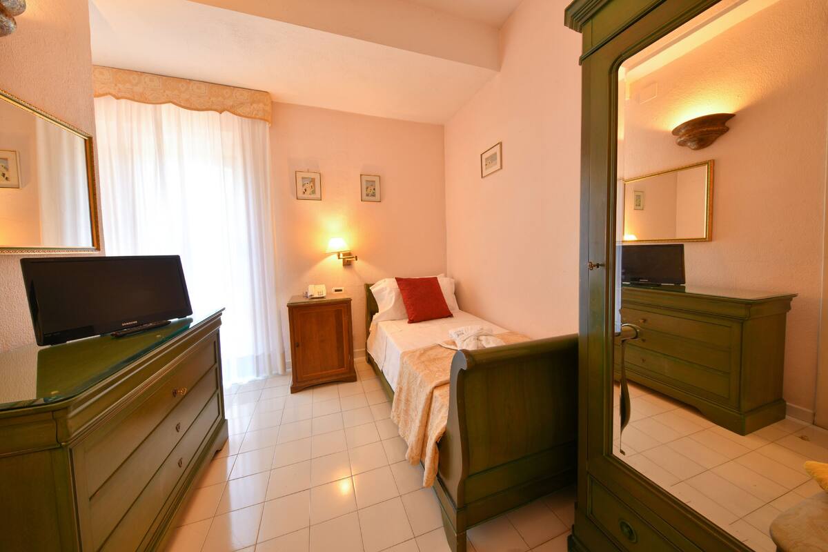 Een slaapkamer met een bed, een dressoir, een nachtkastje, een televisie en een spiegel.
