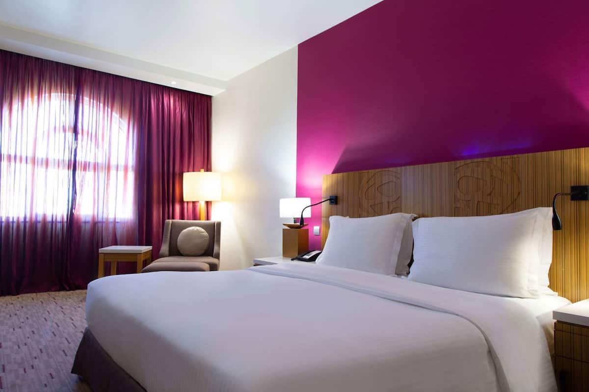 A hotel room with a large bed, a chair, a desk, and a lamp.