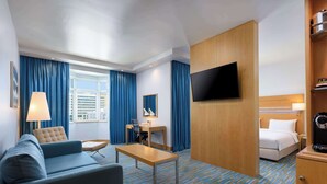 A hotel room with a sofa, a desk, a bed, a television, and a coffee machine.