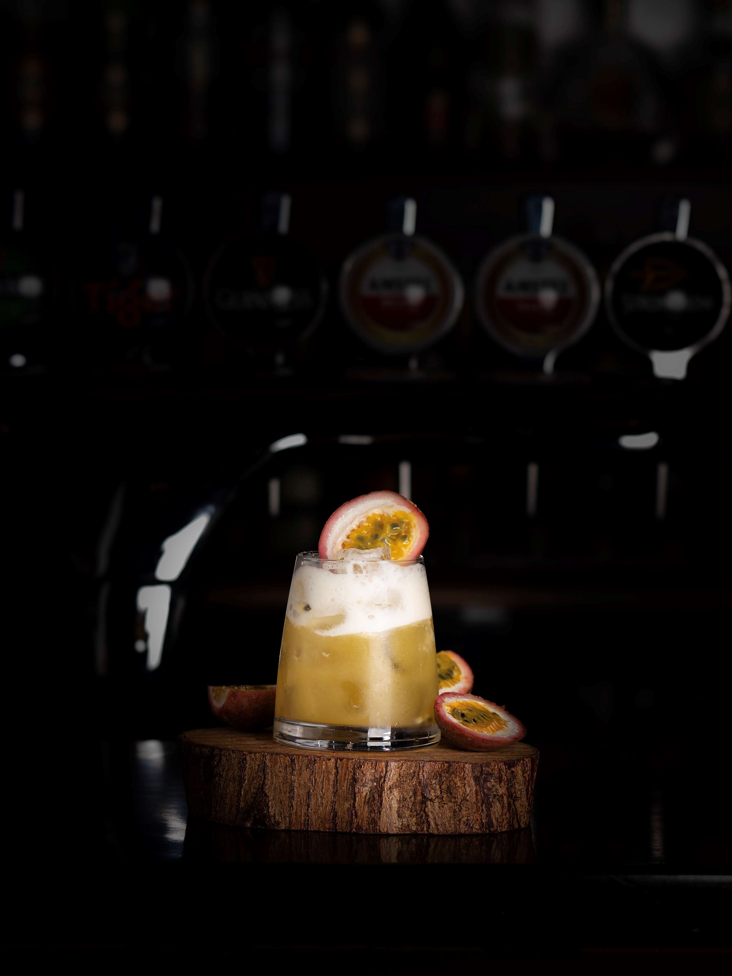 A cocktail with a passion fruit garnish on a wooden bar counter.