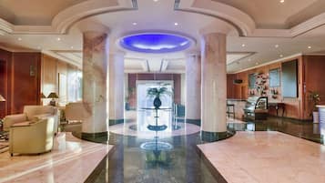 A spacious lobby with marble flooring, a reception desk, and a central fountain.