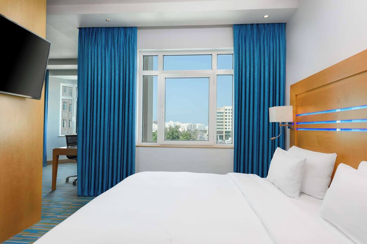 A hotel room with a large bed, a desk, a chair, a TV, and a window with curtains.