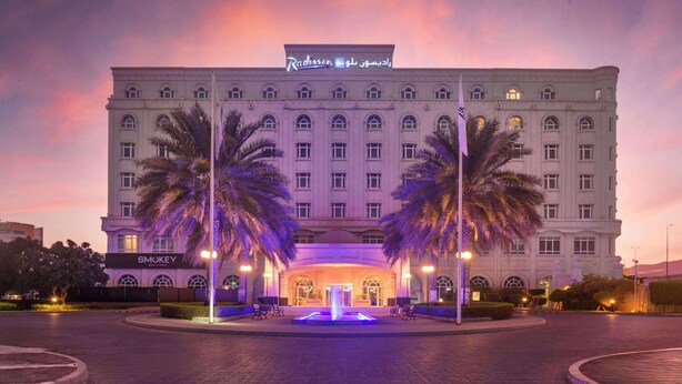 A large hotel with a grand entrance, palm trees, and a fountain.