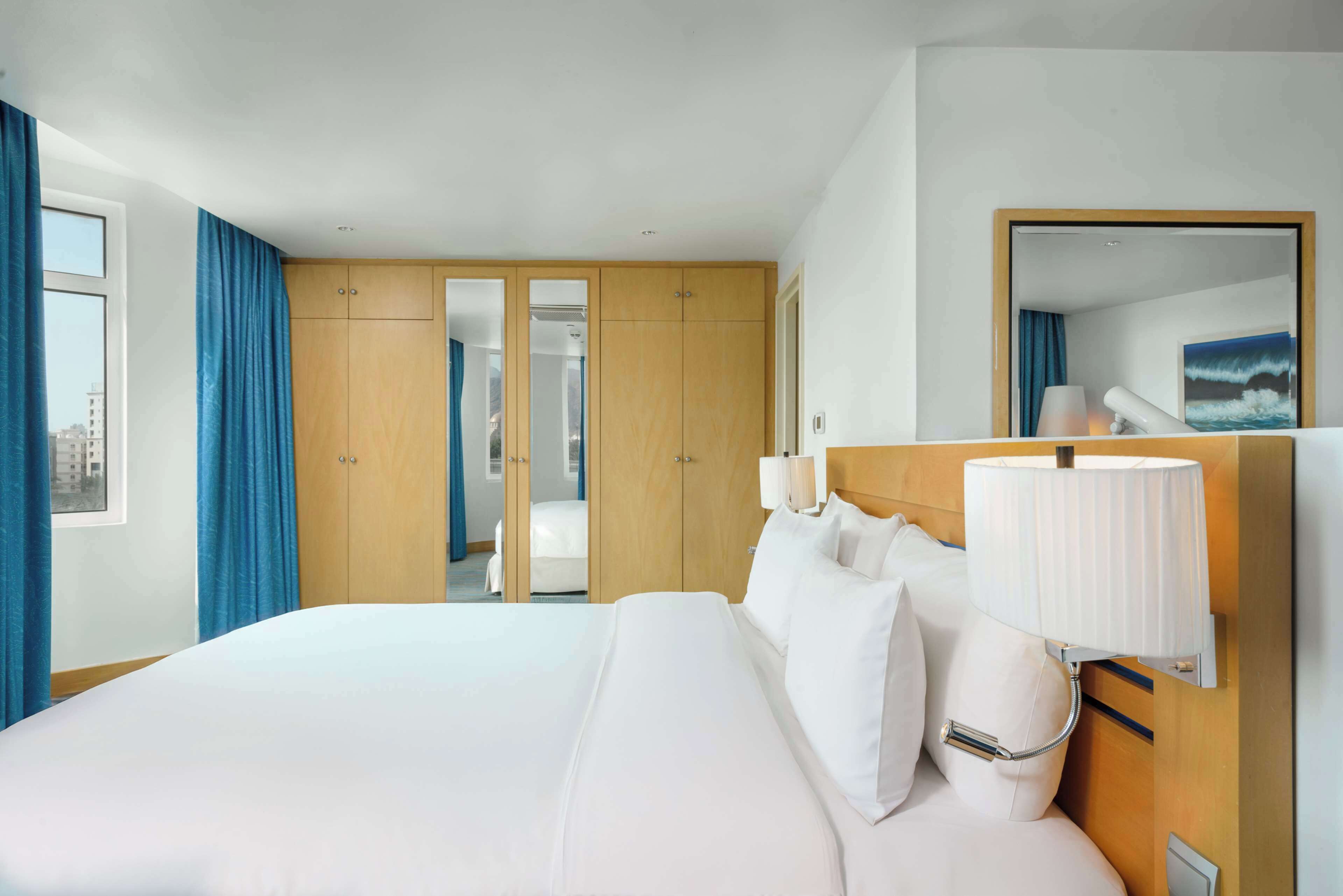 Une chambre d’hôtel avec un grand lit, une armoire en bois, un miroir et une vue sur la ville.