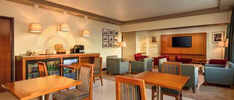 A modern hotel lobby with a bar area, seating arrangements, and a flat-screen TV mounted on the wall.