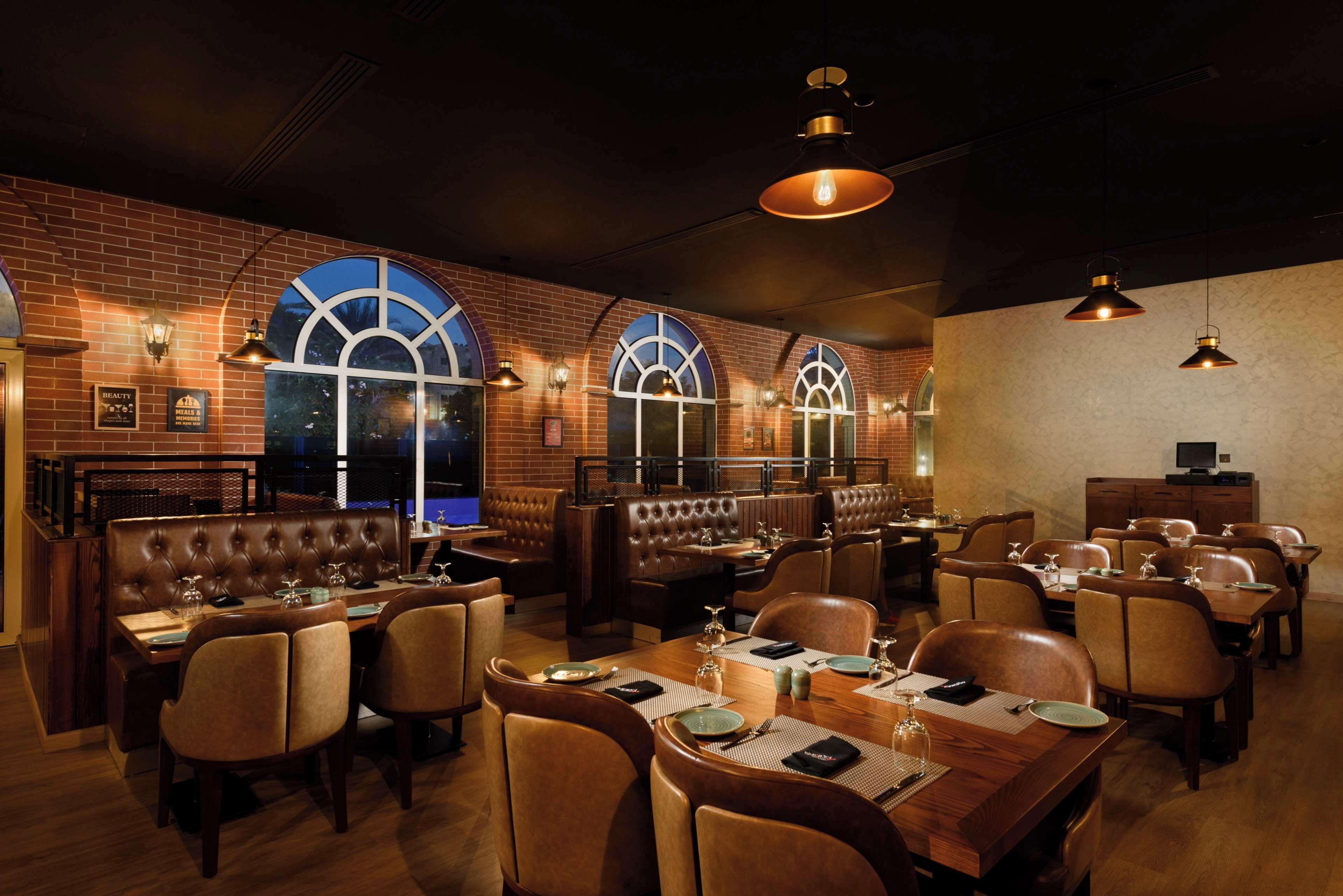 A restaurant with brick walls, arched windows, leather booths, and wooden tables.