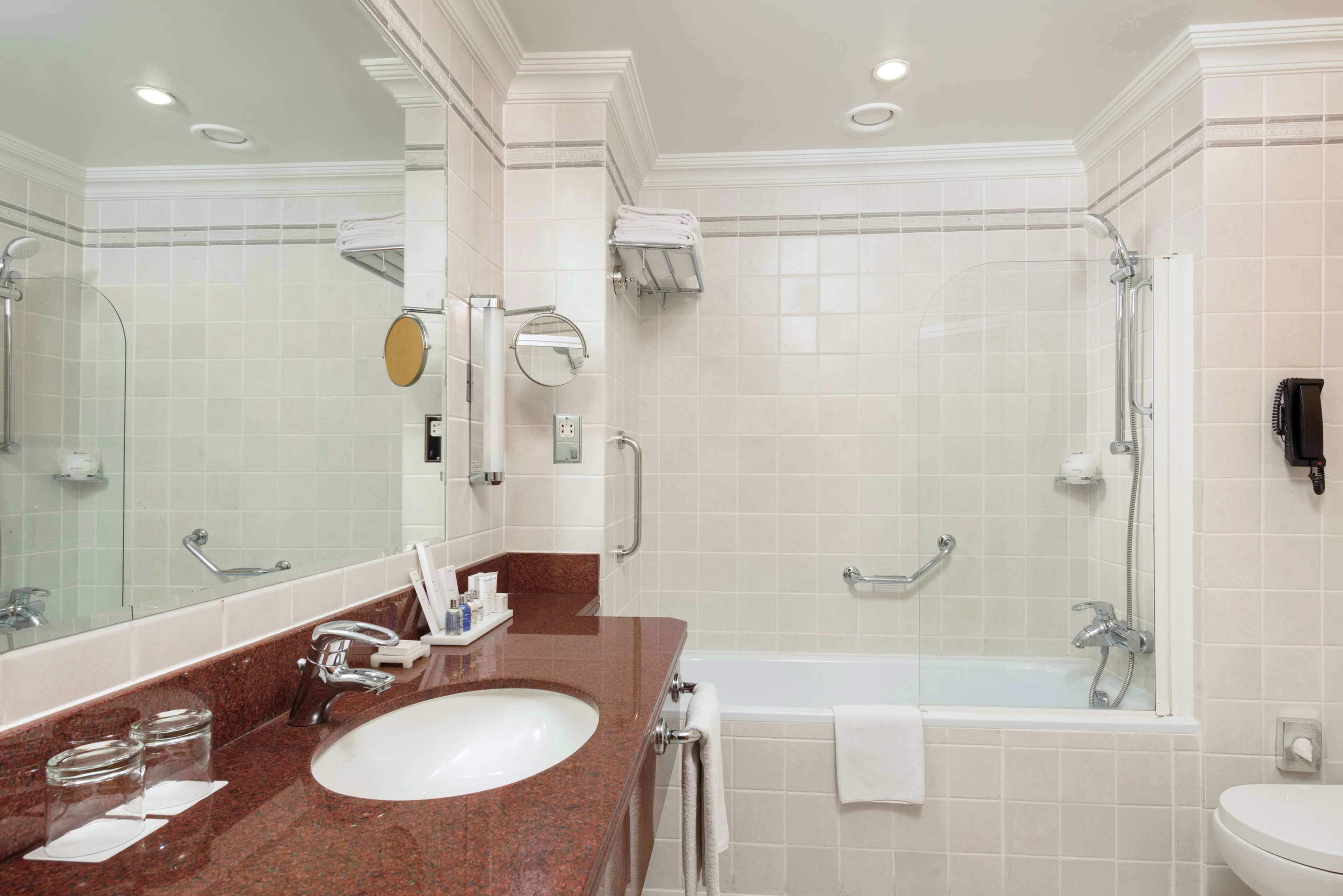 A modern bathroom with a large mirror, a sink, a bathtub, and a toilet.