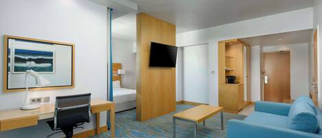 Una habitación de hotel con escritorio, silla, cama, televisor y sofá azul.