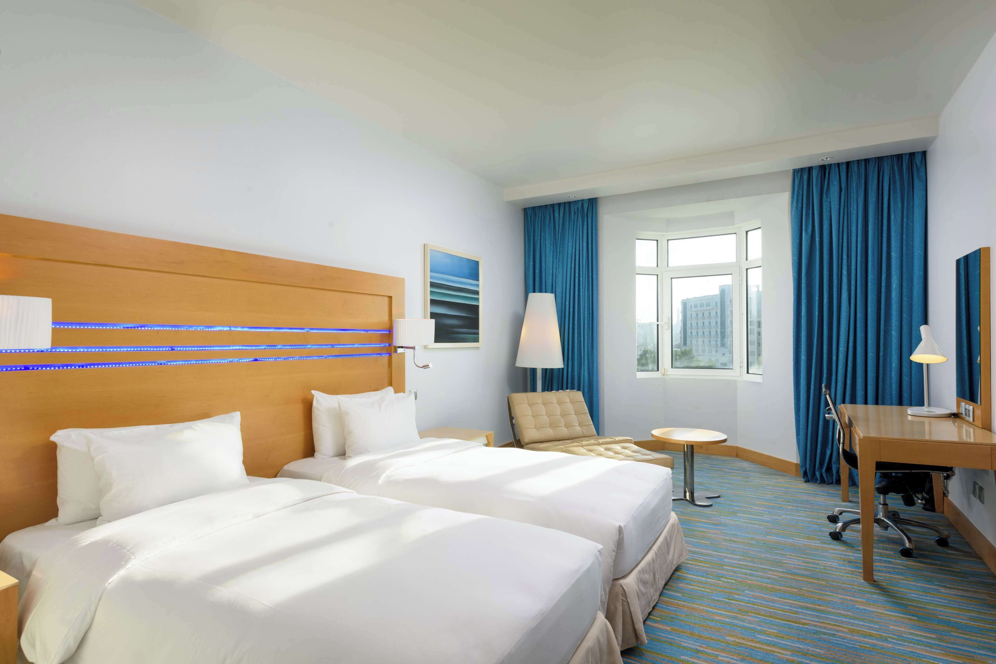 A hotel room with two beds, a desk, a chair, a small table, and a window with curtains.