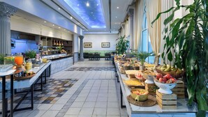 A spacious hotel lobby with a high ceiling, a central seating area, and a buffet with various food items.