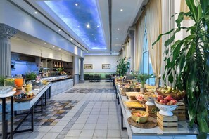 En rymlig hotellobby med högt i tak, en central sittgrupp och en buffé med ett varierat utbud av mat.