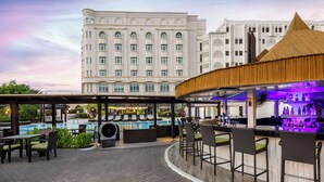 A rooftop bar with a pool, outdoor seating, and a view of a large hotel building. - Radisson Blu Hotel, Muscat (Muscat)