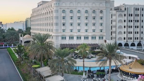 A large, multi-story hotel with a central courtyard featuring palm trees and outdoor seating. - Radisson Blu Hotel, Muscat (Muscat)