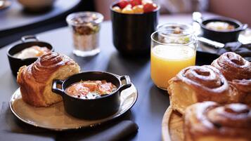 Une table dressée pour le petit-déjeuner avec des croissants, un bol de soupe, un verre de jus d’orange et un saladier de fruits.