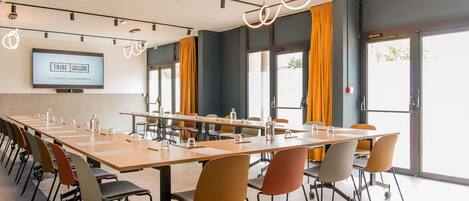 A conference room with a long table, chairs, a TV screen, and curtains.