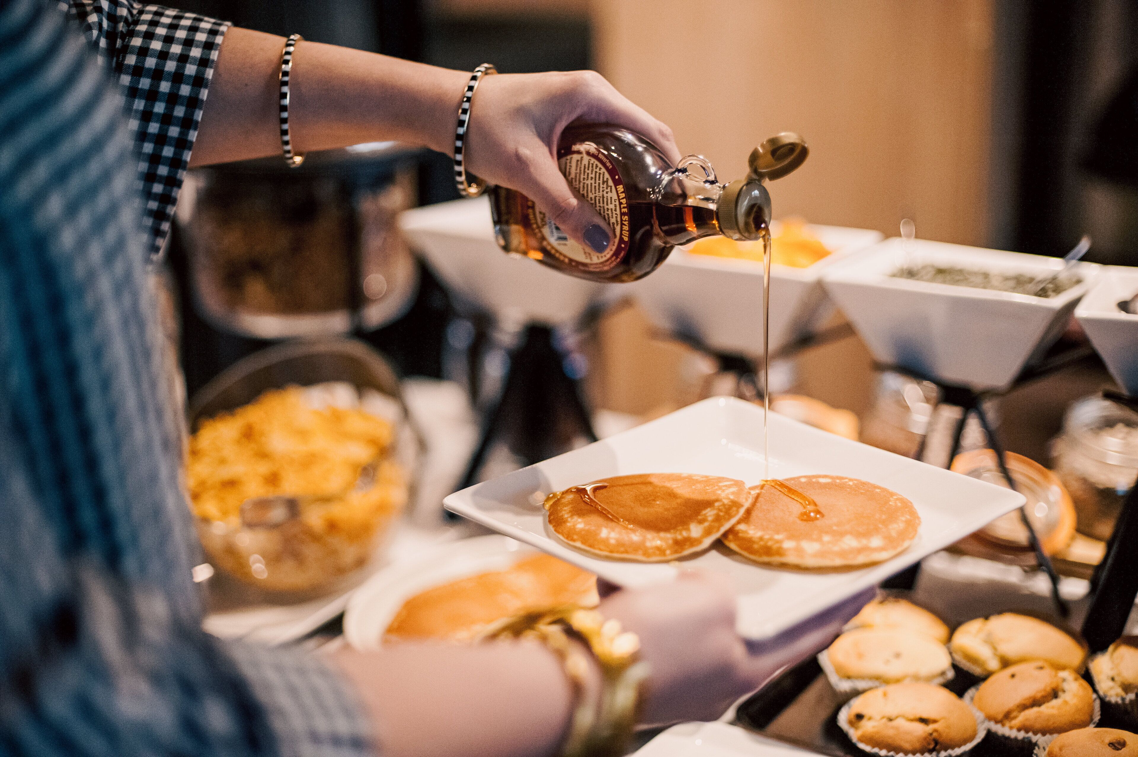 A person pouring syrup onto pancakes on a white plate.