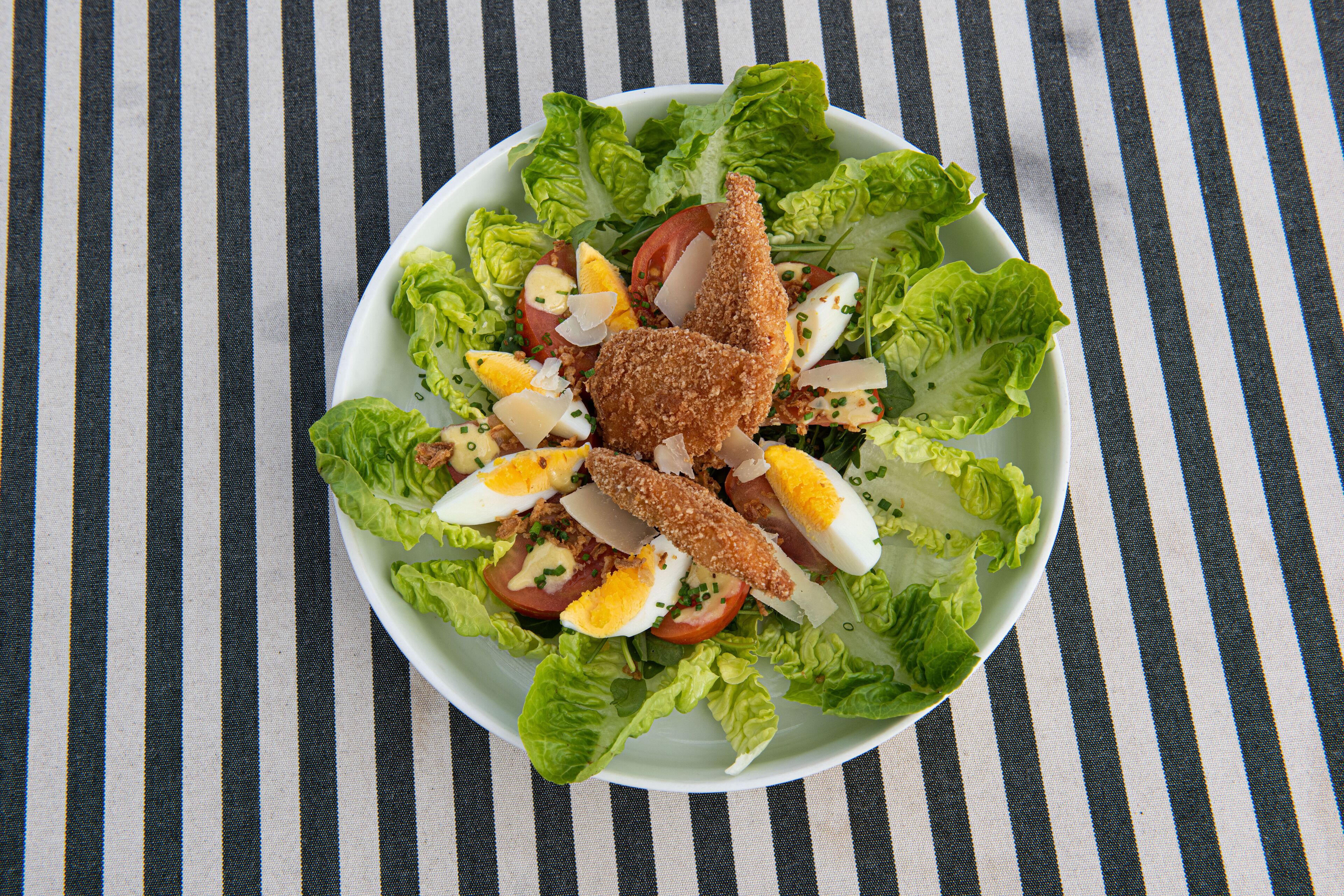 A salad with lettuce, tomatoes, eggs, and breaded chicken on a plate.