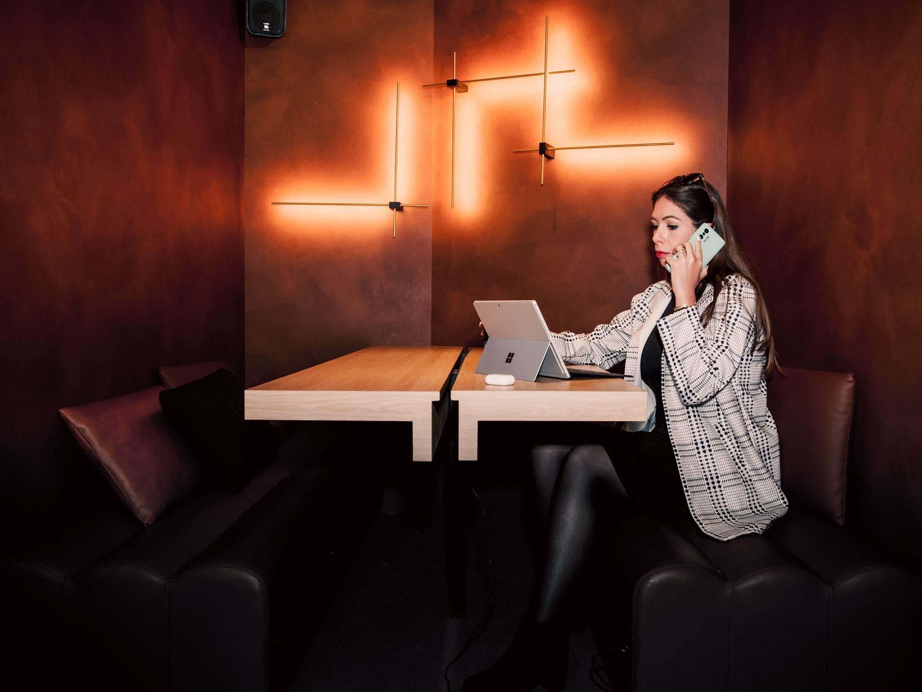 Iemand zit aan een houten tafel met een laptop, in een kamer met een modern design en donkere lederen zitplaatsen.