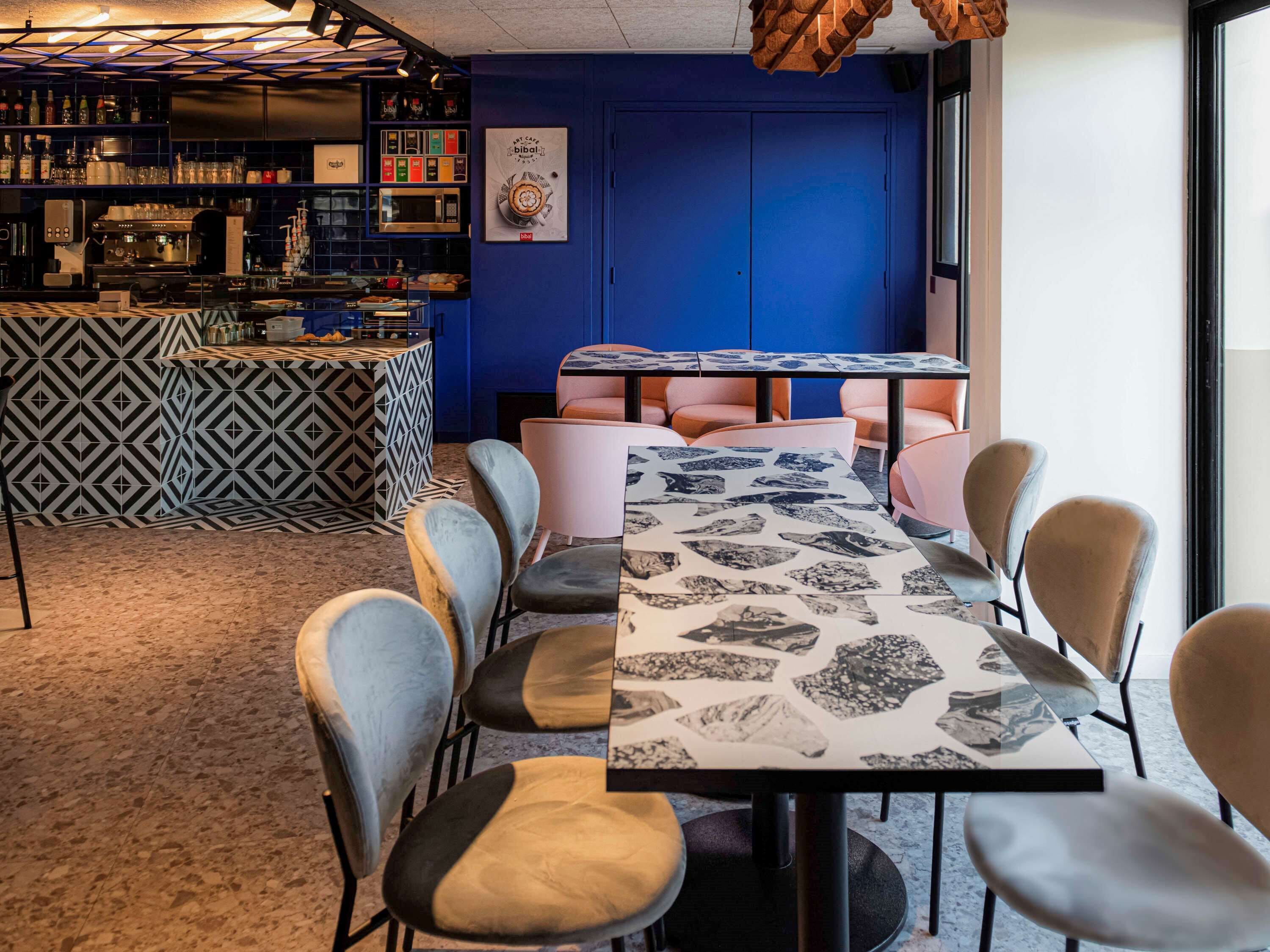 A bar area with a counter, shelves with bottles, and a blue wall. There is a table with chairs in the foreground.