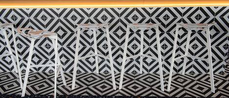 A bar area with a patterned wall and three white bar stools.