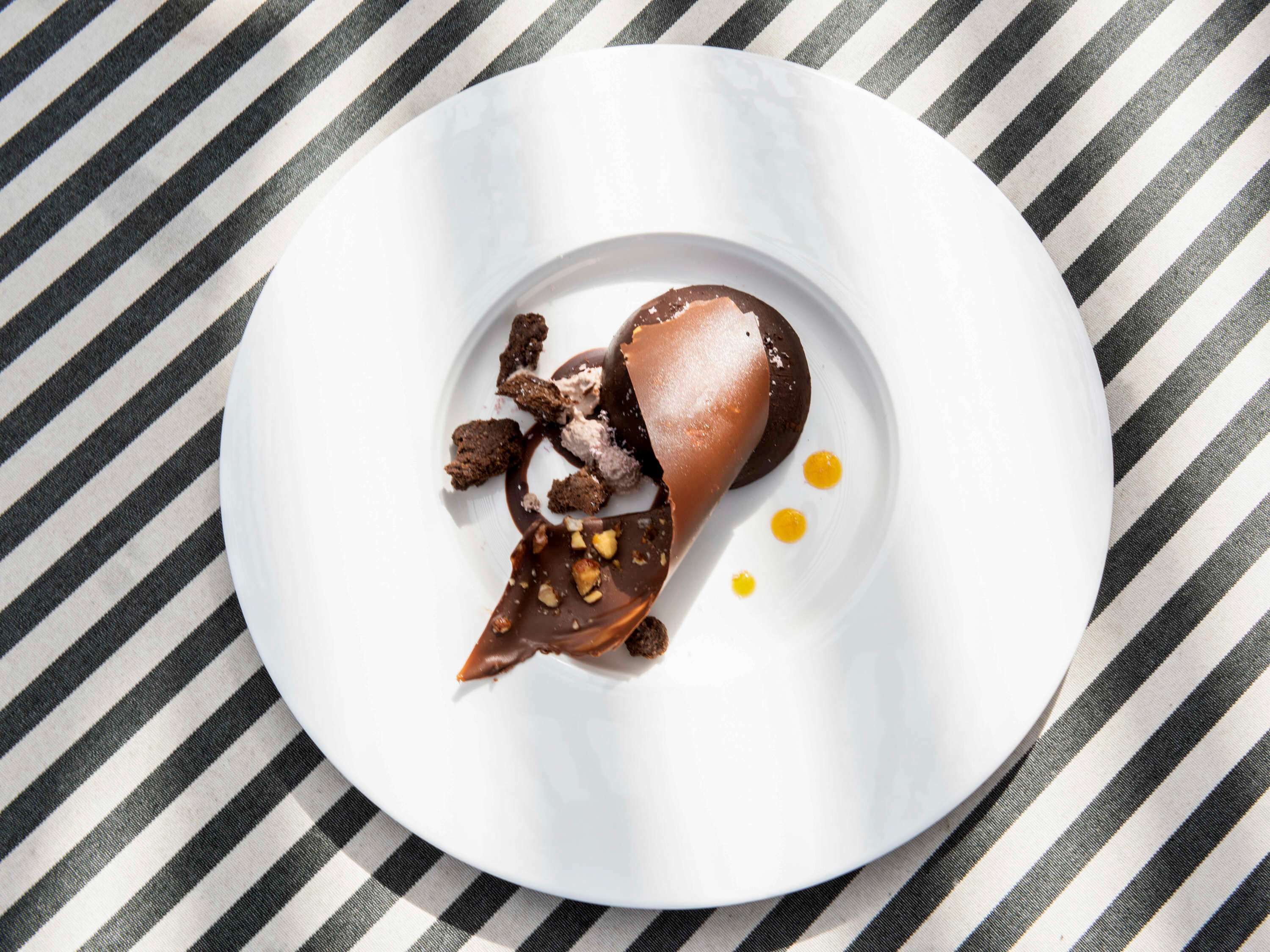 A dessert on a white plate with chocolate and ice cream, placed on a striped tablecloth.
