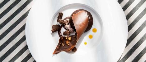 A dessert on a white plate with chocolate and ice cream, placed on a striped tablecloth.