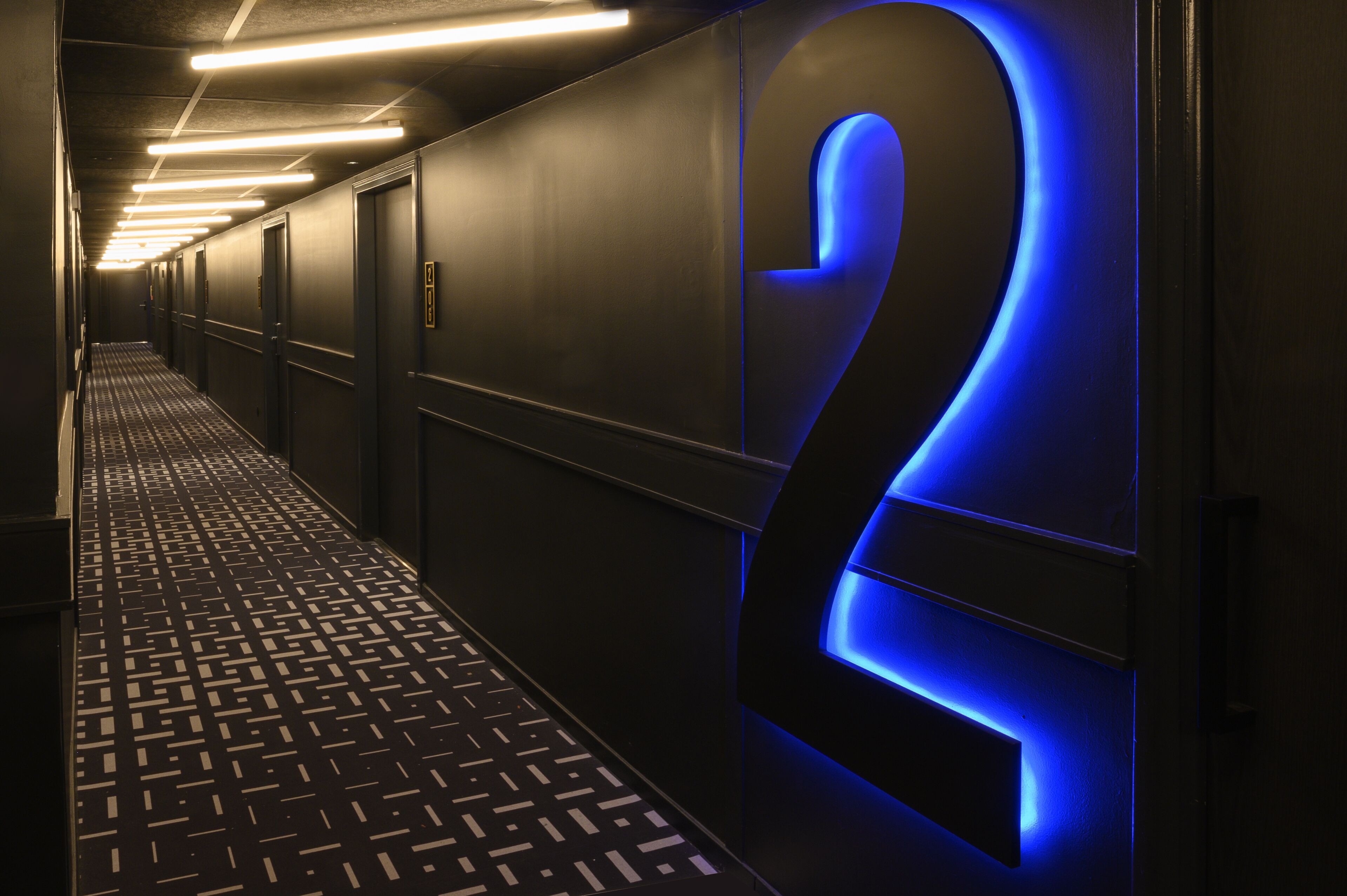 A hallway with a patterned floor, a large illuminated number '2', and overhead lighting.
