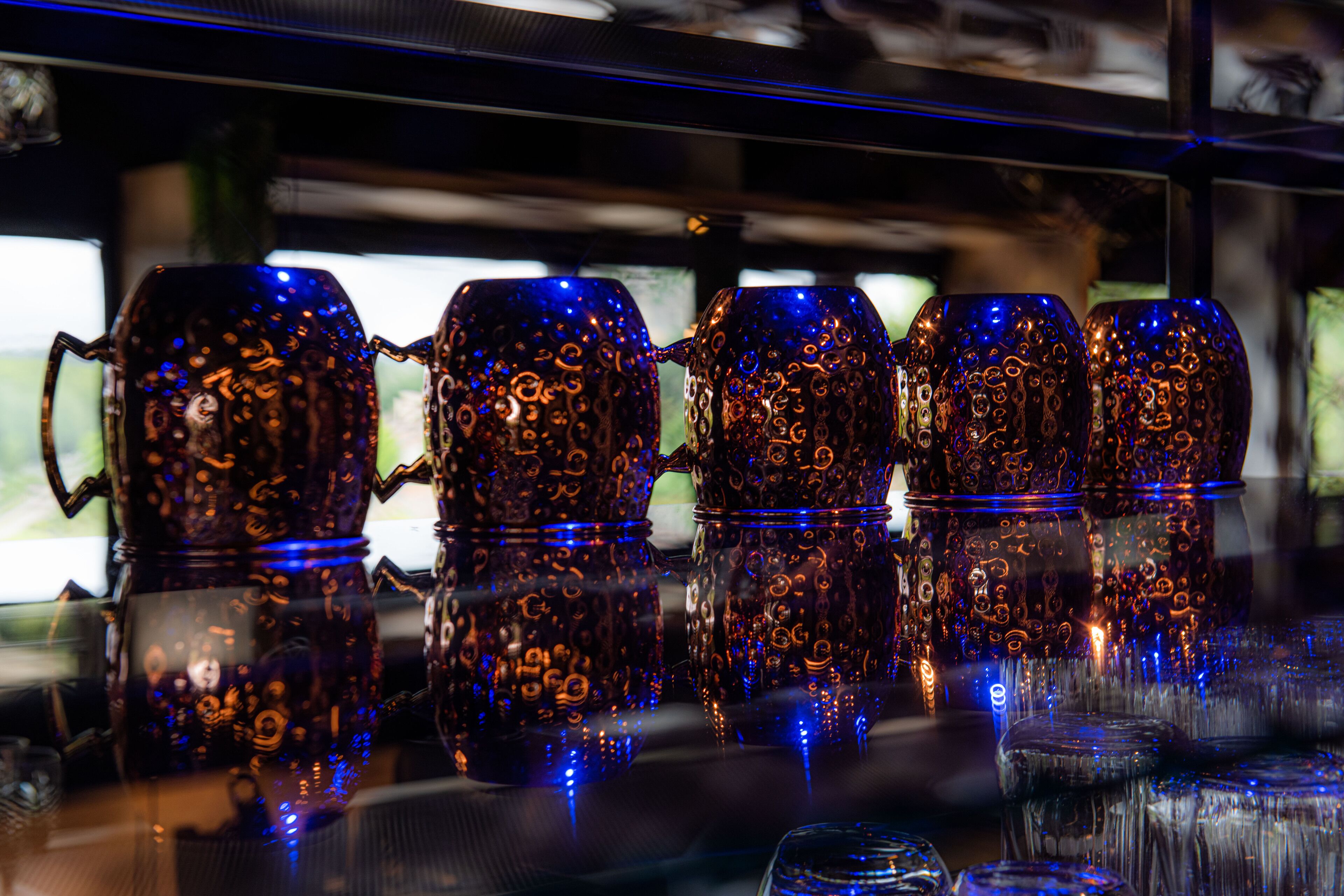 Una zona de bar con una hilera de vasos de vidrio ornamentados y reflectantes sobre una superficie reflectante.