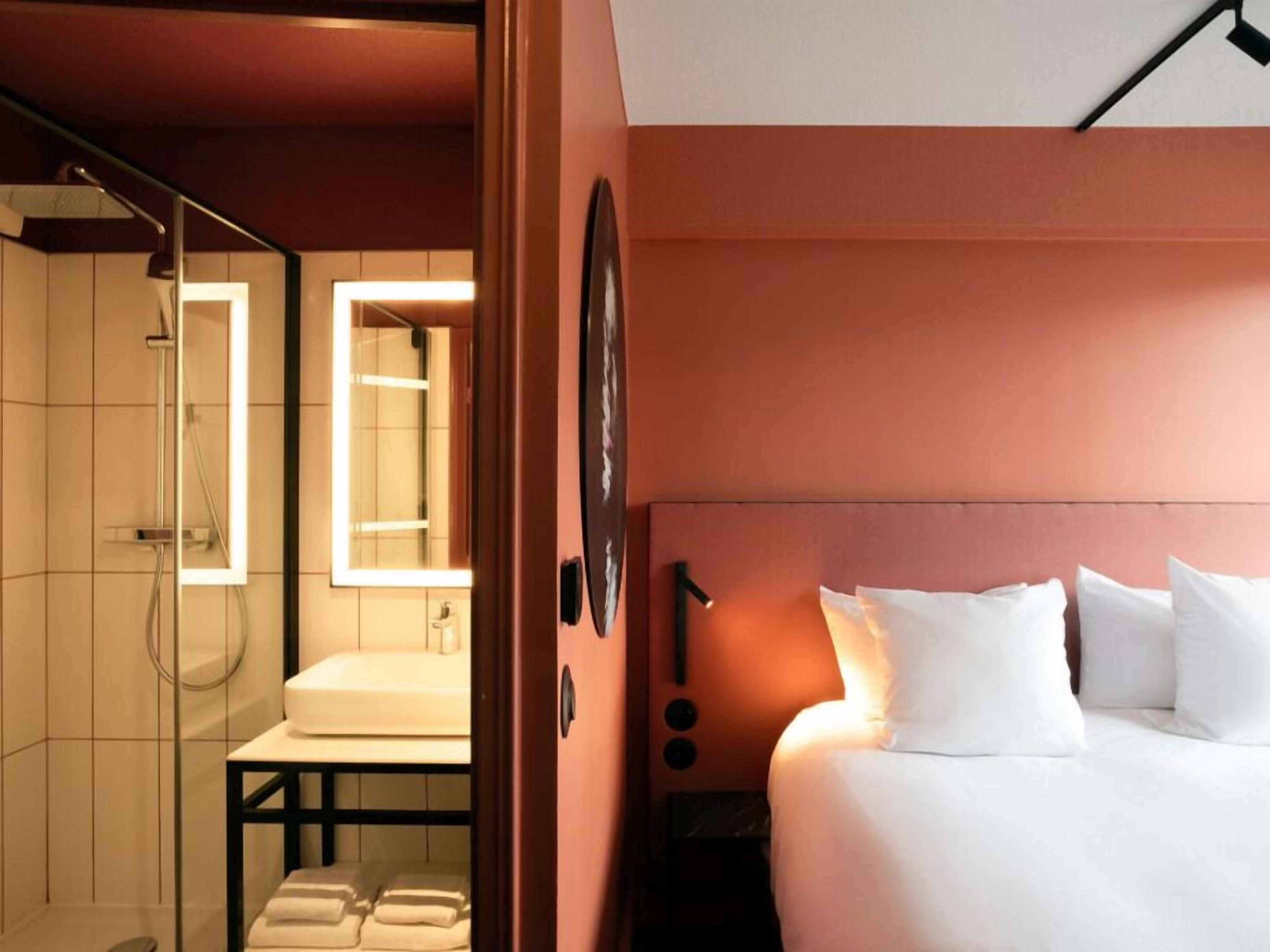 A hotel room with a bed, a bathroom with a shower, and a mirror.