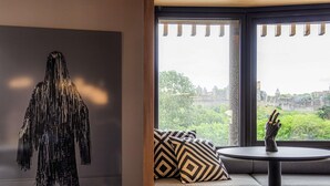 Una habitación con un ventanal grande, un sofá con cojines estampados, una mesita y una escultura colgada en la pared.